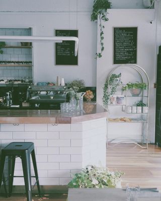 Hunnybee has high ceilings, many plants, and lots of sunlight. Its counter is L-shaped, made of a wood surface, and has white subway tiles down its side panels. There are metal hooks under the counter to hang personal belongings and metal stools to sit on. Behind the counter are two chalkboard menus hanging on the wall and a large espresso machine.